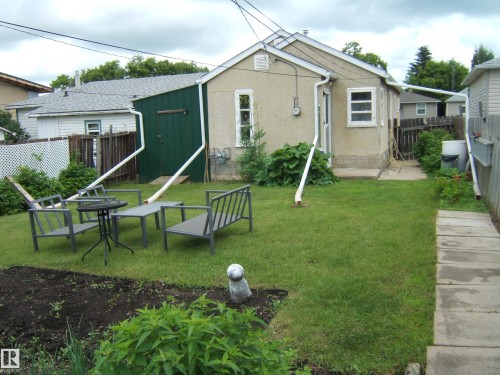 Expansive rear yard featuring a grass lawn, paved walkway, and a designated garden bed - 5530 50 Street, Vegreville, AB 