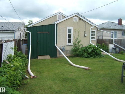 Rear exterior featuring stucco finish, white frame windows, and a green painted wood-panel shed with a dark wood door - 5530 50 Street, Vegreville, AB 
