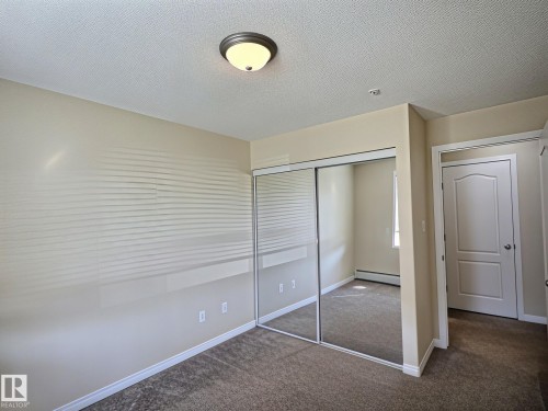 Mirrored closet doors, flush-mount ceiling light fixture, neutral wall paint, and textured ceiling - #111 5350 199 St Nw, Edmonton, AB - Indoor Photo Showing Other Room