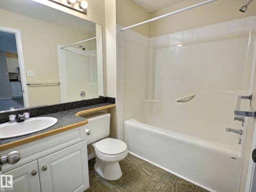 White vanity with a wood-finish countertop, oval sink, and dark speckled counter - #111 5350 199 St Nw, Edmonton, AB - Indoor Photo Showing Bathroom
