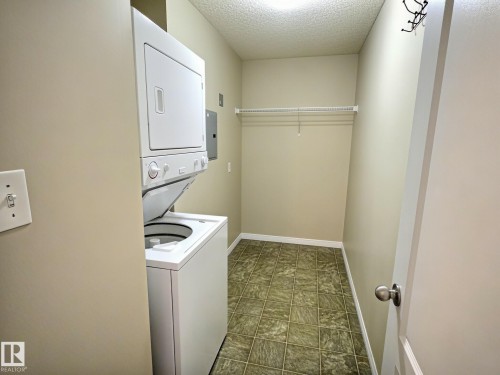 Laundry area with a stacked washer and dryer, patterned floor tiling, and a wire shelving unit - #111 5350 199 St Nw, Edmonton, AB - Indoor Photo Showing Laundry Room