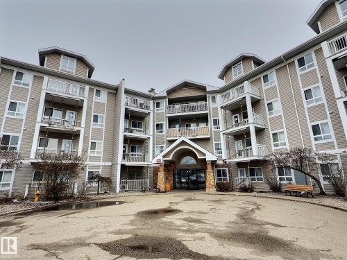 Multi-story building with neutral siding, individual balconies, and a stone-clad entrance - #111 5350 199 St Nw, Edmonton, AB - Outdoor With Facade