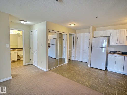 Carpeted and tiled flooring, mirrored closet doors, white kitchen cabinetry, and white appliances - #111 5350 199 St Nw, Edmonton, AB - Indoor Photo Showing Kitchen