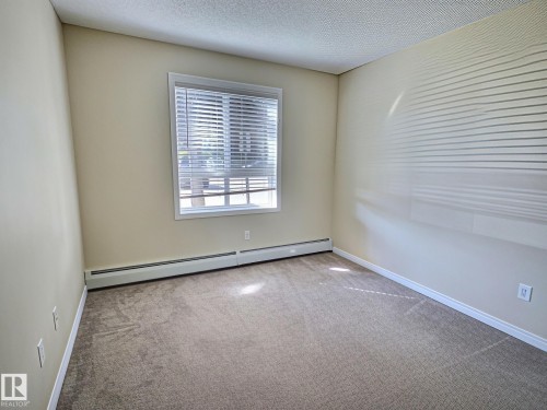 Wall-to-wall carpeting, neutral wall color, and a window with horizontal blinds - #111 5350 199 St Nw, Edmonton, AB - Indoor Photo Showing Other Room
