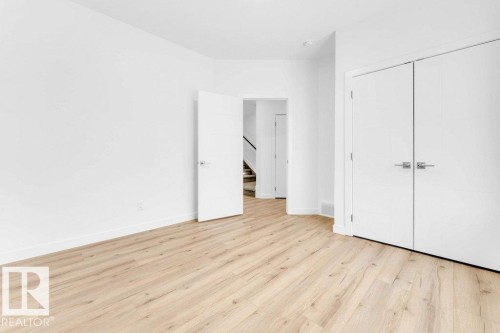 Light wood-finish flooring, white walls, white trim, and modern white doors with contemporary hardware - 182 Pacific Drive, Spruce Grove, AB - Indoor Photo Showing Other Room