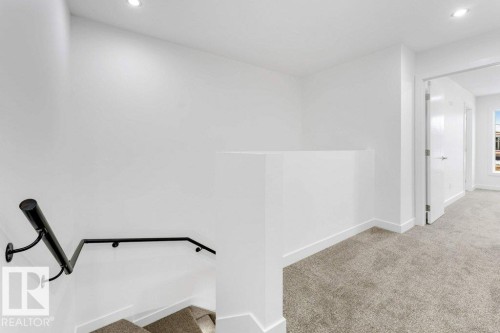 Carpeted hallway with white walls, recessed lighting, and a black metal handrail leading to a lower level - 182 Pacific Drive, Spruce Grove, AB - Indoor Photo Showing Other Room