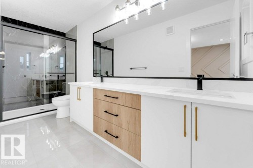 Dual vanity with white countertops, wood-finish and white cabinetry, black fixtures, and a large mirror - 182 Pacific Drive, Spruce Grove, AB - Indoor