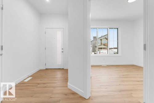 White interior walls, wood-finish flooring, recessed ceiling lighting, a white front door with a frosted glass insert, and a large window with white framing - 182 Pacific Drive, Spruce Grove, AB - Indoor Photo Showing Other Room