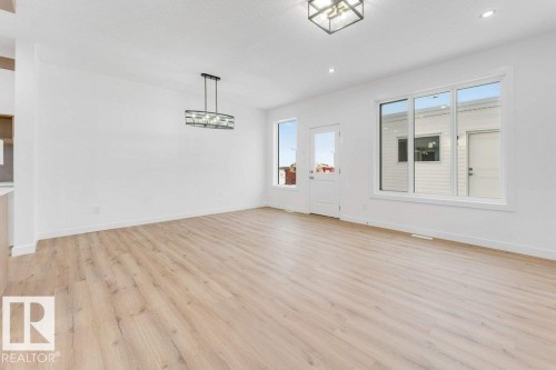 Light wood-finish flooring, white walls, and a contemporary linear chandelier - 182 Pacific Drive, Spruce Grove, AB - Indoor Photo Showing Other Room