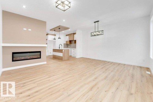 Open-concept living space featuring wood-finish flooring, a linear electric fireplace with mantel, recessed lighting, and a kitchen island with pendant lighting - 182 Pacific Drive, Spruce Grove, AB - Indoor With Fireplace