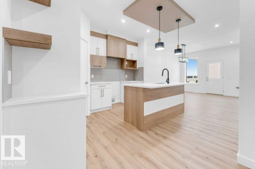 Modern open-concept kitchen and living space featuring a wood-finish island with waterfall countertop edge, white cabinetry with wood-tone accents, stainless steel appliances, pendant lighting, and light wood-finish flooring throughout - 182 Pacific Drive, Spruce Grove, AB - Indoor Photo Showing Kitchen