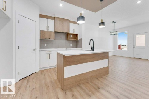 Modern kitchen featuring an island with a white countertop and integrated sink, two-tone cabinetry, and wood-finish flooring - 182 Pacific Drive, Spruce Grove, AB - Indoor Photo Showing Kitchen