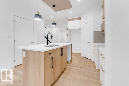 Kitchen island with a white countertop and integrated sink, black gooseneck faucet, light wood-finish cabinetry, and recessed lighting - 182 Pacific Drive, Spruce Grove, AB - Indoor