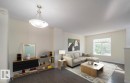 Expansive living area with dark wood-finish flooring, a large window, and a contemporary ceiling light fixture - #66 465 Hemingway Rd Nw, Edmonton, AB 