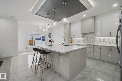 Contemporary kitchen featuring a center island with countertop seating, stainless steel appliances, and a tiled backsplash - 4820 174 Avenue Nw, Edmonton, AB - Indoor Photo Showing Kitchen With Upgraded Kitchen