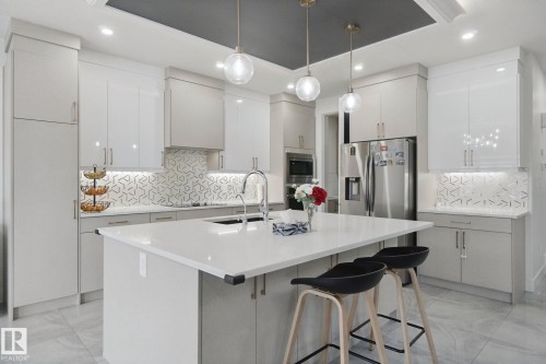 Modern kitchen featuring a large central island, pendant lighting, stainless steel appliances, and a geometric-patterned backsplash - 4820 174 Avenue Nw, Edmonton, AB - Indoor Photo Showing Kitchen With Upgraded Kitchen