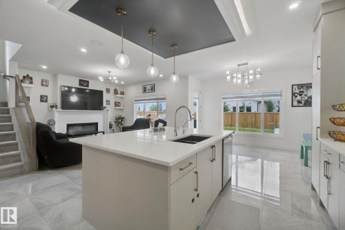 Open-concept living area with a kitchen island featuring an integrated sink, a built-in electric fireplace, and a tray ceiling with recessed lighting - 4820 174 Avenue Nw, Edmonton, AB - Indoor Photo Showing Kitchen With Double Sink With Upgraded Kitchen