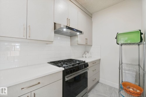 White subway tile backsplash, white countertops, built-in overhead cabinetry, and stainless steel range hood - 4820 174 Avenue Nw, Edmonton, AB - Indoor Photo Showing Kitchen With Upgraded Kitchen