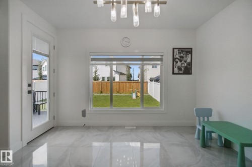 White interior featuring a large window, a glass-paneled door, and a multi-light linear chandelier - 4820 174 Avenue Nw, Edmonton, AB - Indoor Photo Showing Other Room