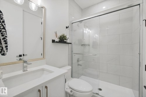 White vanity with integrated sink, chrome faucet, framed mirror, and a walk-in shower with glass enclosure and tiled walls - 4820 174 Avenue Nw, Edmonton, AB - Indoor Photo Showing Bathroom