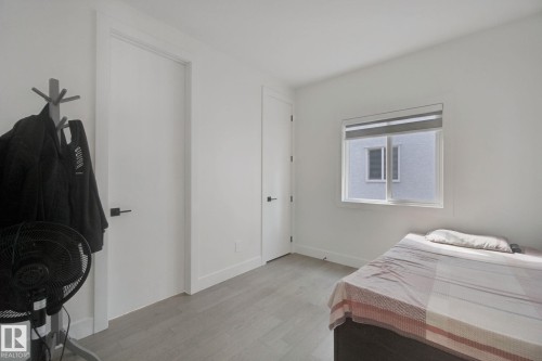 Light-filled room featuring a single window with a roller shade, wood-finish flooring, white walls, and modern black door hardware - 4820 174 Avenue Nw, Edmonton, AB - Indoor Photo Showing Bedroom