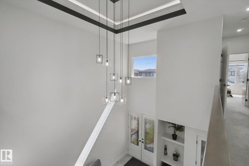 Two-story ceiling with a multi-light chandelier, double entry doors with decorative glass inserts, and built-in shelving - 4820 174 Avenue Nw, Edmonton, AB - Indoor Photo Showing Other Room