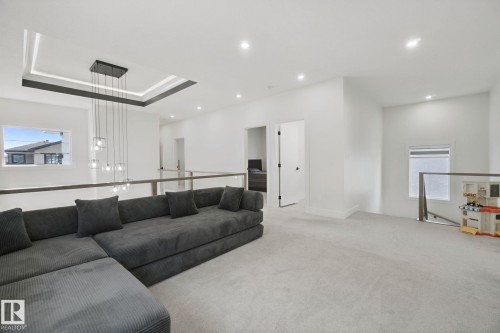 Recessed lighting, contemporary chandelier with multiple pendants, tray ceiling with dark trim, glass railing, and light-colored carpeting - 4820 174 Avenue Nw, Edmonton, AB - Indoor Photo Showing Living Room