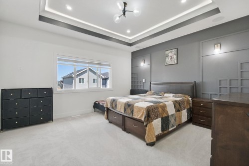 Tray ceiling with recessed lighting and a central fixture, window with roller shades, and wall sconces on a paneled accent wall - 4820 174 Avenue Nw, Edmonton, AB - Indoor Photo Showing Bedroom