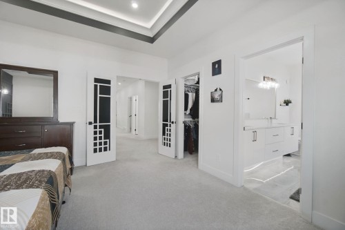 Spacious primary suite featuring carpeted flooring, dual walk-in closets with mirrored doors, an ensuite bathroom with frameless glass shower enclosure, dual vanity sinks, and recessed ceiling lighting - 4820 174 Avenue Nw, Edmonton, AB - Indoor