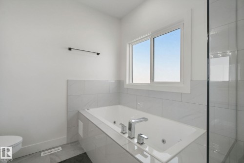 Recessed soaking tub with polished chrome fixtures, white subway tile surround, and a large window - 4820 174 Avenue Nw, Edmonton, AB - Indoor Photo Showing Bathroom