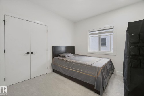 Recessed window with roller blinds, light-toned carpeting, and a built-in closet with double doors featuring black hardware - 4820 174 Avenue Nw, Edmonton, AB - Indoor Photo Showing Bedroom