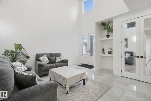 High ceilings, transom window, double entry doors with decorative glass, built-in shelving, and large format floor tiling - 4820 174 Avenue Nw, Edmonton, AB - Indoor Photo Showing Living Room