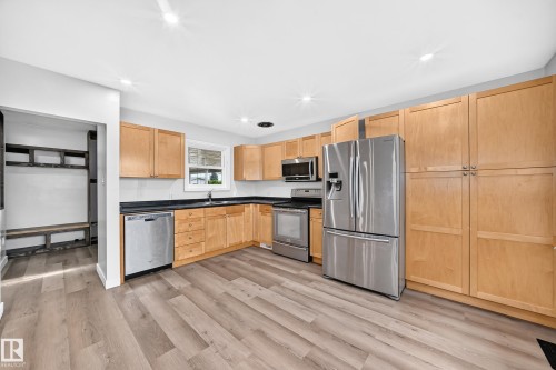 Updated kitchen featuring wood-finish flooring, light-toned cabinetry, dark countertops, and stainless steel appliances - 7603 130 Avenue Nw, Edmonton, AB - Indoor Photo Showing Kitchen