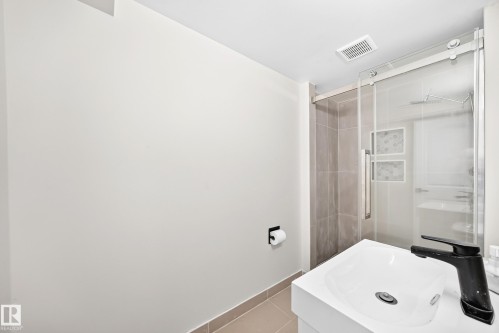 Floating vanity with integrated sink, matte black single-handle faucet, glass-enclosed shower with subway tile surround, and decorative accent tile - 7603 130 Avenue Nw, Edmonton, AB - Indoor Photo Showing Bathroom