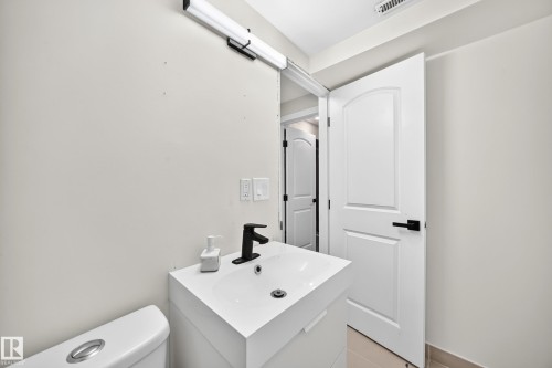 White vanity with an integrated sink and matte black faucet, wall-mounted light fixture, and white paneled door with black hardware - 7603 130 Avenue Nw, Edmonton, AB - Indoor Photo Showing Bathroom