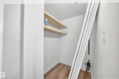 Spacious walk-in closet featuring wood-finish flooring, white painted walls, and natural wood floating shelves for organized storage and display - 7603 130 Avenue Nw, Edmonton, AB - Indoor