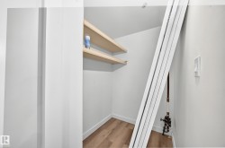 Spacious walk-in closet featuring wood-finish flooring, white painted walls, and natural wood floating shelves for organized storage and display - 