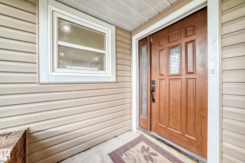 Welcoming covered entry featuring horizontal vinyl siding, a solid wood six-panel door with sidelights, and a picture window with white trim - 7603 130 Avenue Nw, Edmonton, AB - Outdoor With Exterior
