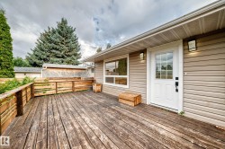 Expansive wood deck with a wood railing, beige horizontal siding, white exterior door with glass panels, and a large exterior window - 