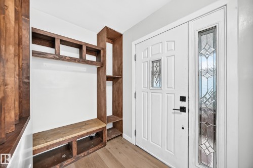 Entryway featuring wood-finish flooring, a built-in wood-finish storage unit with shelving and bench, and a white paneled door with decorative glass inserts - 7603 130 Avenue Nw, Edmonton, AB - Indoor Photo Showing Other Room