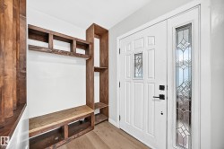 Entryway featuring wood-finish flooring, a built-in wood-finish storage unit with shelving and bench, and a white paneled door with decorative glass inserts - 