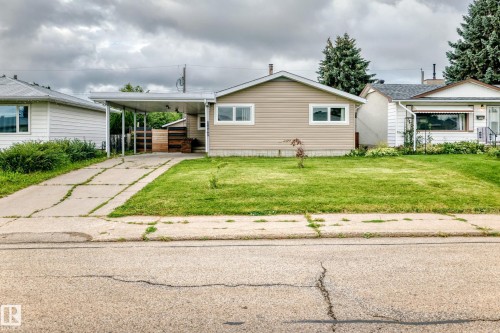Single-story home featuring light-colored siding, a front lawn, and a paved driveway leading to a carport - 7603 130 Avenue Nw, Edmonton, AB - Outdoor