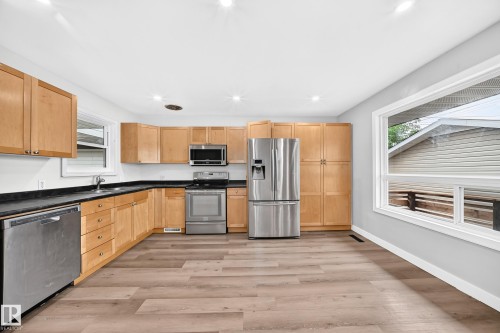 Full kitchen with wood-finish cabinetry, stainless steel appliances, dark countertops, and wood-finish flooring - 7603 130 Avenue Nw, Edmonton, AB - Indoor Photo Showing Kitchen With Double Sink