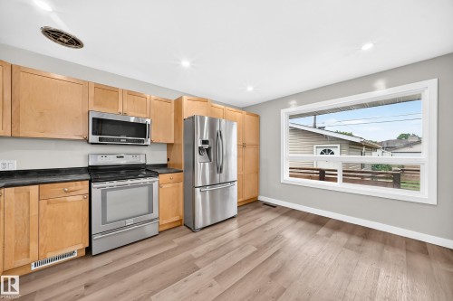 Kitchen featuring wood-finish flooring, light wood cabinetry, stainless steel appliances, and a large window - 7603 130 Avenue Nw, Edmonton, AB - Indoor Photo Showing Kitchen