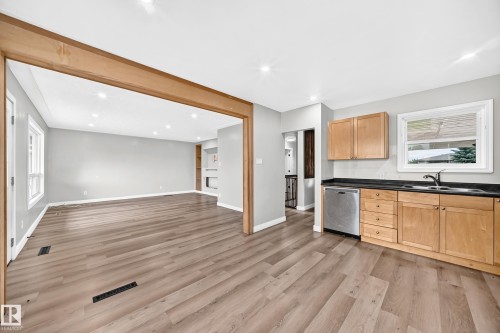 Open concept kitchen and living area featuring wood-finish flooring, recessed lighting, wood cabinetry, stainless steel dishwasher, and a built-in fireplace - 7603 130 Avenue Nw, Edmonton, AB - Indoor Photo Showing Kitchen With Double Sink