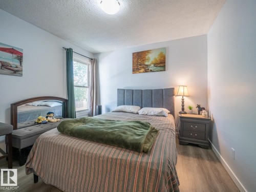 Light wood-finish flooring, a window with drapery, a paneled headboard, and a two-drawer nightstand - #No 510 Abbottsfield Rd Nw Nw, Edmonton, AB - Indoor Photo Showing Bedroom