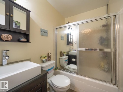 White rectangular vessel sink with a polished chrome faucet, dark wood-finish vanity cabinet, wall-mounted mirrored medicine cabinet, and a shower-over-tub with sliding glass doors - #No 510 Abbottsfield Rd Nw Nw, Edmonton, AB - Indoor Photo Showing Bathroom