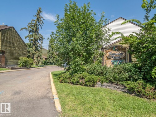 Community entrance featuring a sign with decorative accents, surrounded by mature landscaping and a well-maintained lawn - #No 510 Abbottsfield Rd Nw Nw, Edmonton, AB - Outdoor