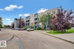 Multi-story building with a neutral and blue exterior, featuring multiple private balconies, a glass-enclosed stairwell, and a paved parking area - 