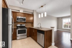 Stainless steel appliances, warm wood cabinetry, neutral countertops, tile backsplash, and dark wood-finish flooring - 